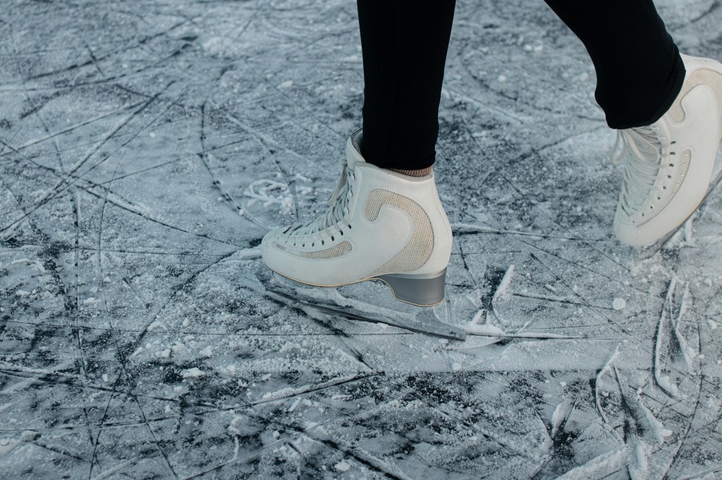 The feet of an ice skater wearing white skates ready to do a spin.